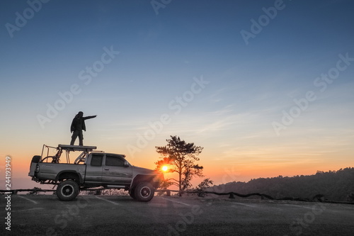 sunset at Huai Nam Dang National Park, beautiful silhouette of a man standing on roof-rack of his car with colorful red light in the sky background, Huai Nam Dang in Chiang Mai, northern of Thailand. © Yuttana Joe