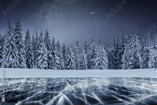 Fototapeta Naklejka Na Ścianę i Meble -  Dairy Star Trek above the winter woods. Cracks on the surface of the blue ice near hills of pines. Frozen lake in mountains. Carpathian Ukraine Europe