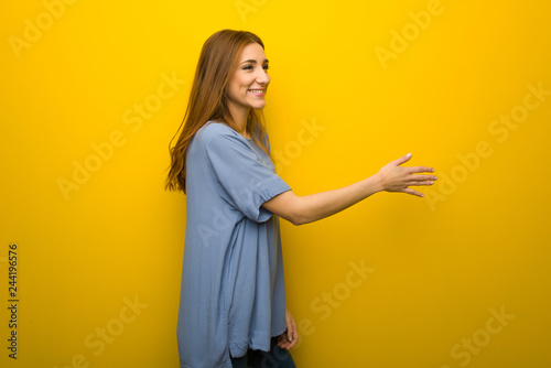 Young redhead girl over yellow wall background handshaking after good deal © luismolinero