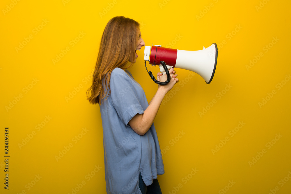 Young redhead girl over yellow wall background shouting through a megaphone to announce something in lateral position Young redhead girl over yellow wall background shouting through a megaphone to announce something in lateral position