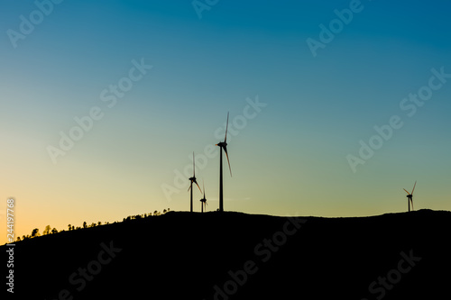 Silhouette view of a wind turbines on top of mountains, sunset sky
