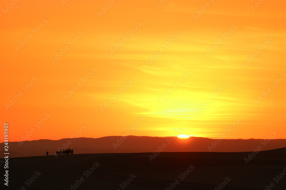 Incredible sunset over the sand dunes of Huacachina desert with the silhouette of tourists dune buggy, Ica region, Peru