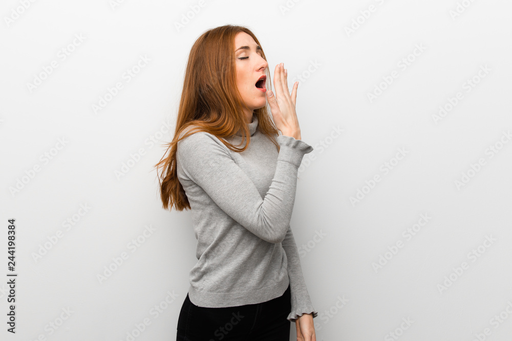 Redhead girl over white wall yawning and covering wide open mouth with hand Redhead girl over white wall yawning and covering wide open mouth with hand