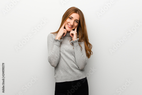 Redhead girl over white wall smiling with a happy and pleasant expression