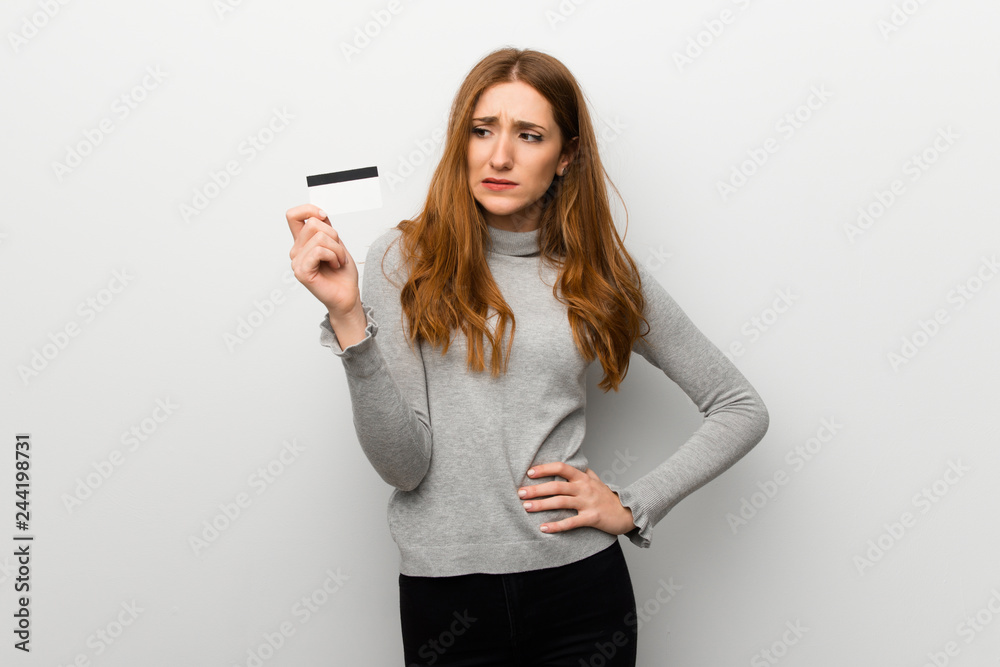 Redhead girl over white wall taking a credit card without money Redhead girl over white wall taking a credit card without money