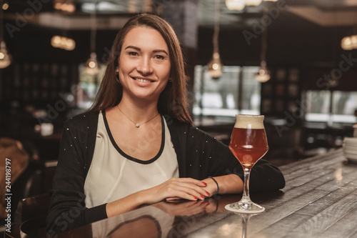 Fotografía Lovely young woman smiling to the camera, resting at the local bar, having beer at the counter