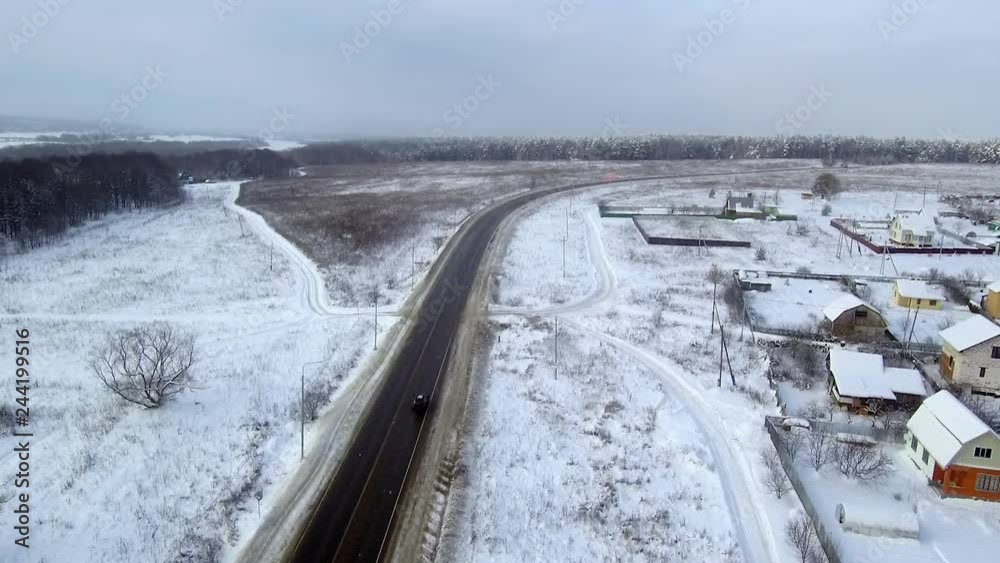 Black car rides on highway in snowfall. Rides in long right turn in to winter forest. Aerial view. Black car rides on highway in snowfall. Rides in long right turn in to winter forest. Aerial view.
