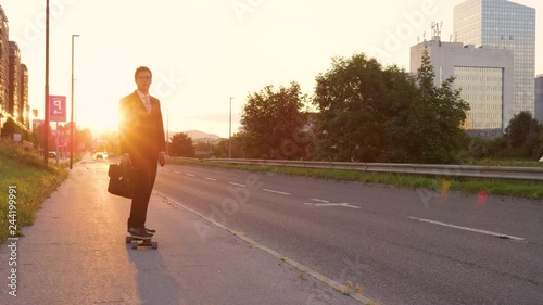 SLOW MOTION, LENS FLARE: Cool sporty businessman going home from work on his e-skateboard. Cheerful yuppie cruising through the city on a sunny summer evening. Happy young man enjoying his ride home. photo