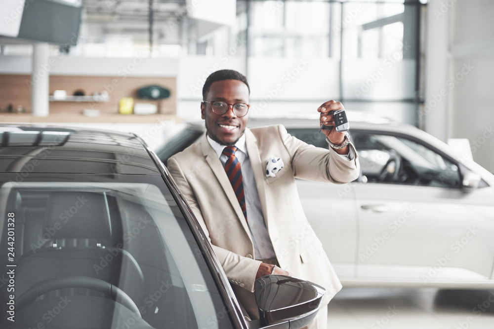 Handsome black man in dealership is hugging his new car and smiling Handsome black man in dealership is hugging his new car and smiling