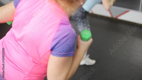 Senior obese woman with dumbbells practicing tae bo exercises, kicking forward with legs in the gym photo