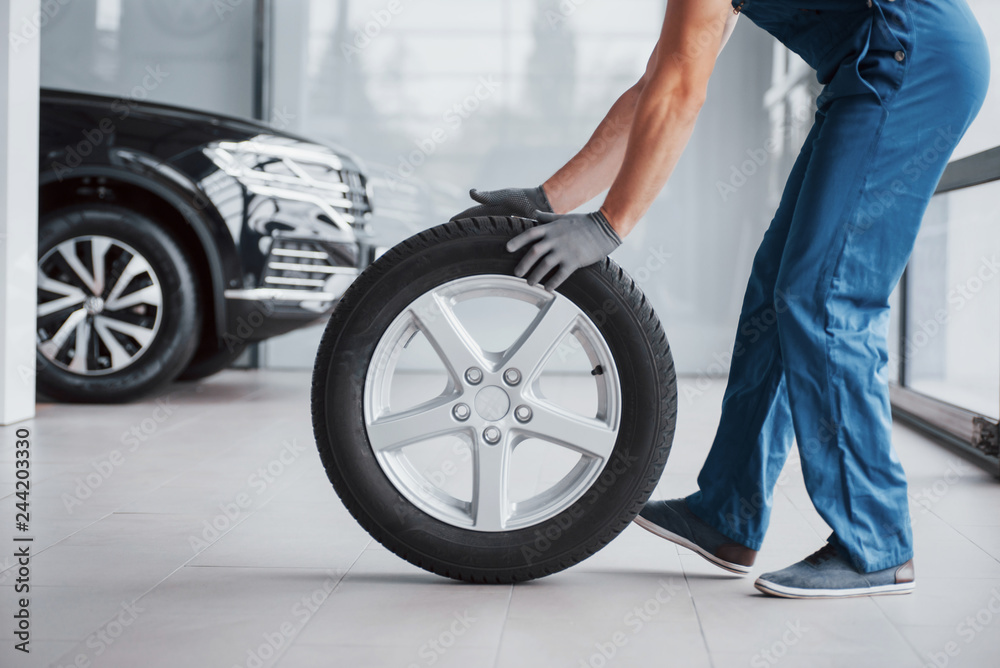 Obraz premium Mechanic holding a tire tire at the repair garage. replacement of winter and summer tires