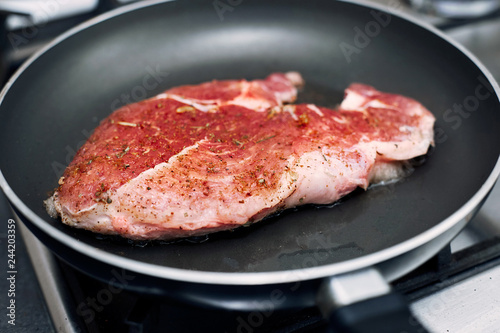 Raw pork chop in a frying pan with rosemary, pepper and salt.