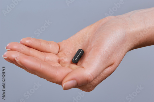 Hand holding black activated carbon capsule for food poisoning treatment - Image.Vitamins And Dietary Supplements.