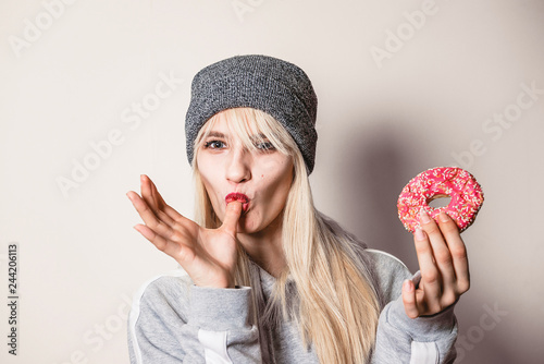 Beautiful girl eating a pink donut, licking the finger. Beauty fashion youth, enjoying the food, eat colorful donut. Diet diet concept. Junk food, weight loss.
