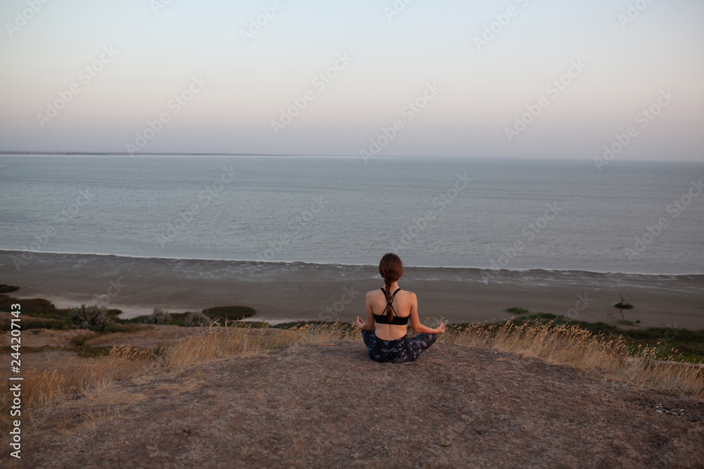 Unrecognizable young woman Practicing Yoga in Lotus pose sitting on the edge of rock against of see. Padmasana