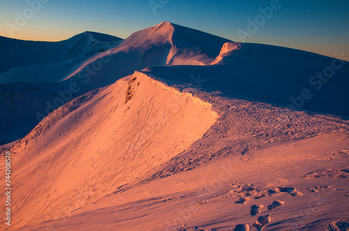 Beautiful alpine panoramic views of the snow-capped mountains. Magic orange and purple Sunrise in the mountains in a winter frosty day. Location Carpathian national park, Ukraine, Europe. Ski resort.
