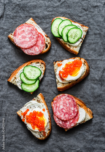 Appetizer sandwiches with red caviar, egg, sausage, cucumber and cream cheese on grey background, top view