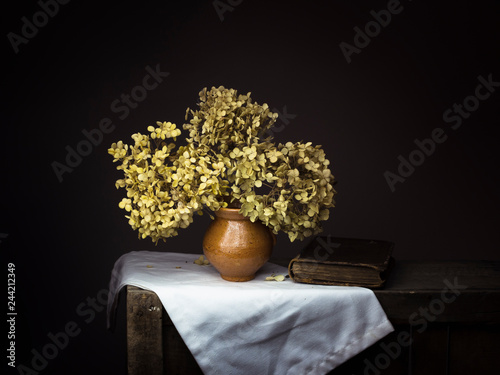 Dramatic chiaroscuro style photo of dried hydrangea flowers with old book on dark background. Melancholy still life with copy space. photo