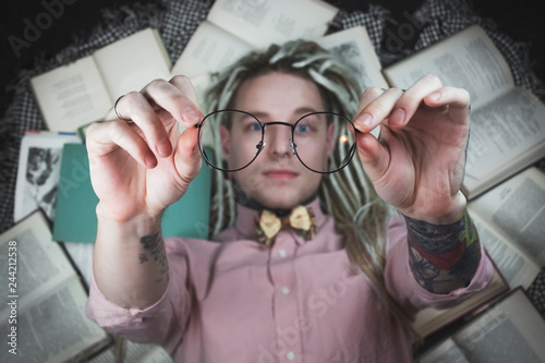 EDITORIAL Tattooed man with dreads laying on books wearing glasses for education