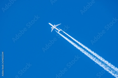 An airplane and a trail from an airplane in a blue sky