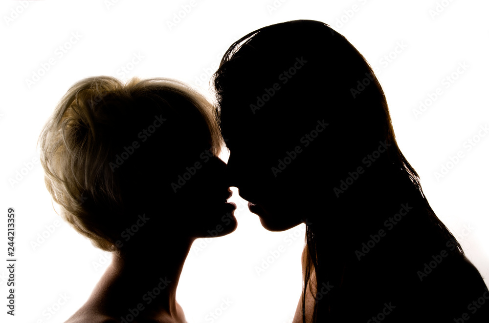 Two girls kissing in front of a white wall.