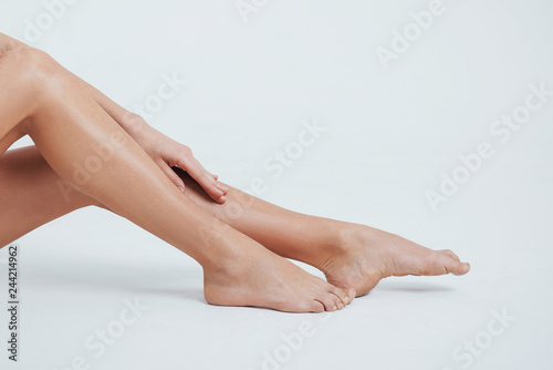 Close up photo of female smooth legs with hand on it and white background behind © standret