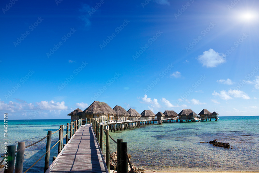 authentic houses with a straw roof over water of the blue sea and the sky with clouds. Polynesia...