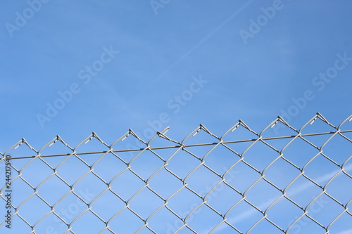 A close up photograph of a section of wire fencing  against a blue sky.  Security  safety concept. Barrier