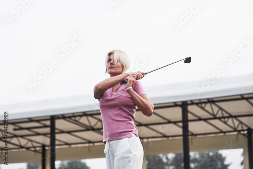 Blonde adult woman tracking the golf ball while holding stick after a hit