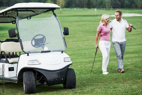 The golf cart with lovely couple walking near the vehicle and smiling