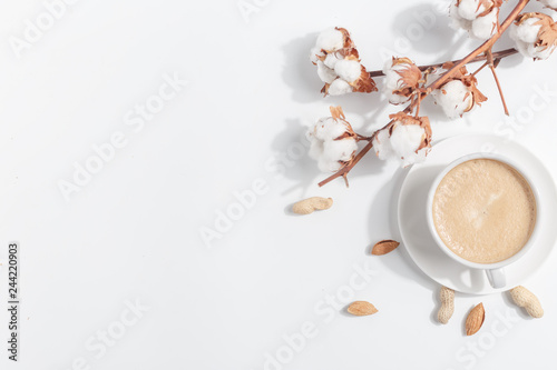 A branch of cotton and a cup of coffee with milk on a light background. Top view. Copy space.