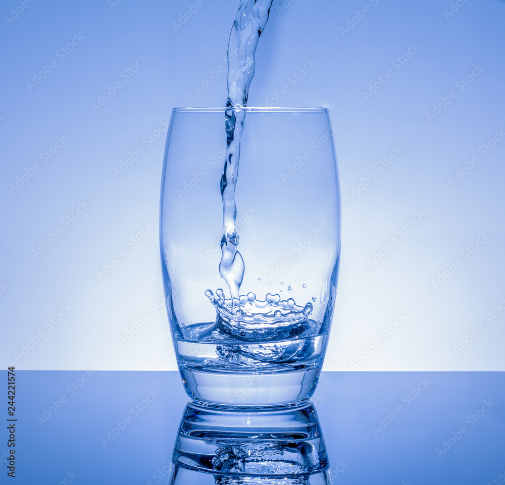 Frisches Getränk in das Glas giessen - Wasser spritzt im Glas auf blauem Hintergrund Frisches Getränk in das Glas giessen - Wasser spritzt im Glas auf blauem Hintergrund