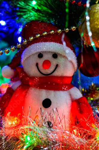 Close-up of a winter white toy snowman with Christmas tinsel in the background