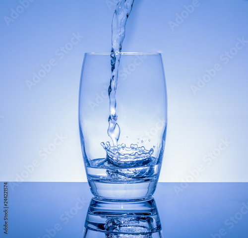 Frisches Getränk in das Glas giessen - Wasser spritzt im Glas auf blauem Hintergrund