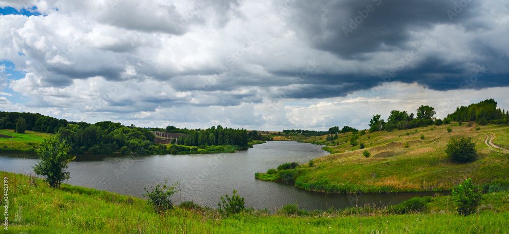 Cloudy windy summer panoramic landscape with small river.