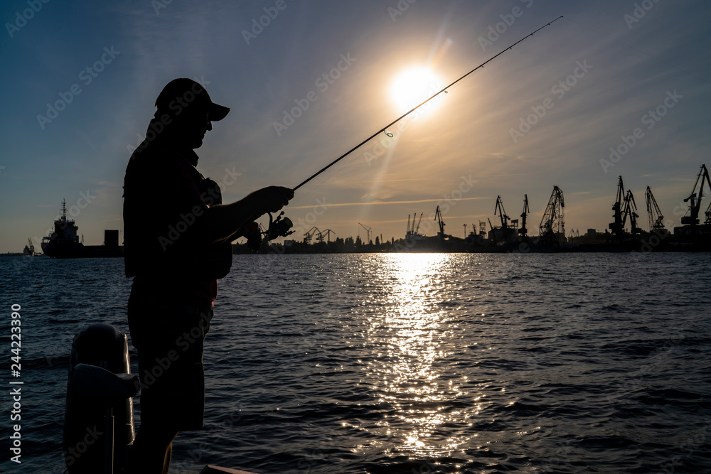 Urban fishing concept. Silhouette of fisherman on industrial seaport city background.