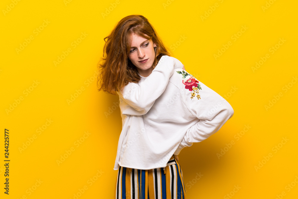 Young redhead woman over yellow wall suffering from pain in shoulder for having made an effort Young redhead woman over yellow wall suffering from pain in shoulder for having made an effort