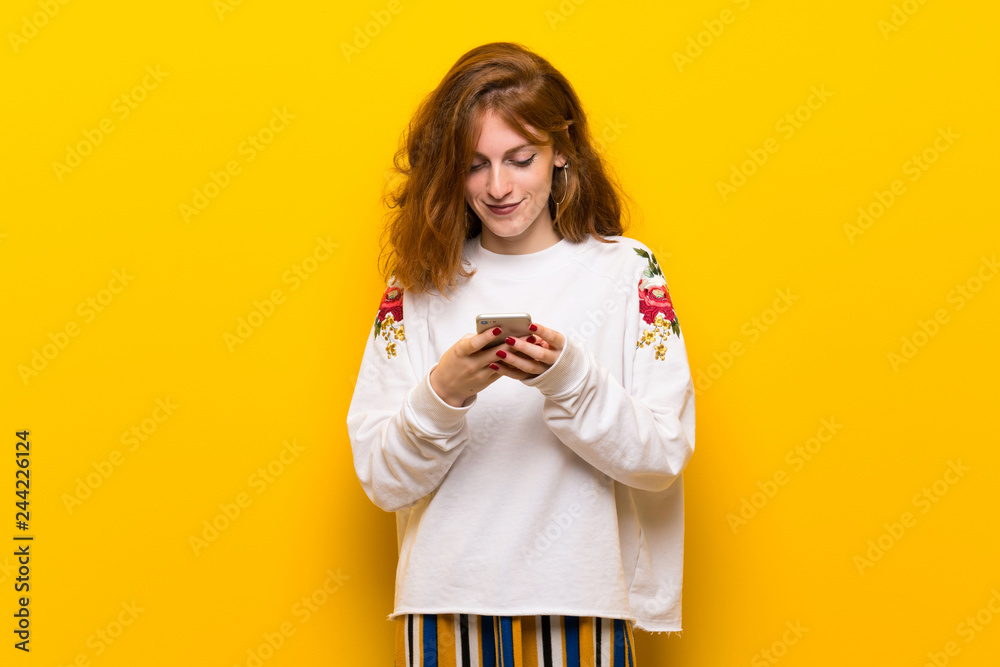 Young redhead woman over yellow wall sending a message with the mobile Young redhead woman over yellow wall sending a message with the mobile