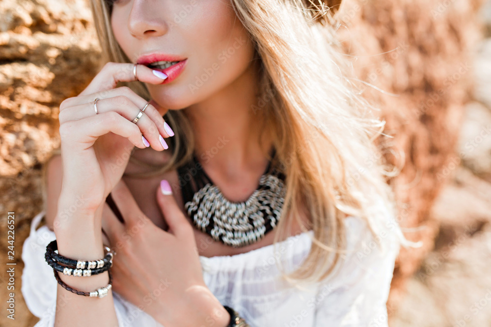 Close-up portrait of attractive blonde girl with long hair on rock background. She keeps finger on lips.