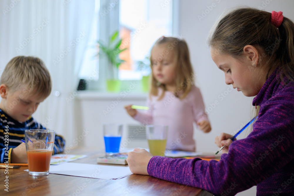 Group of cute children from one family is painting on the paper sitting together Group of cute children from one family is painting on the paper sitting together