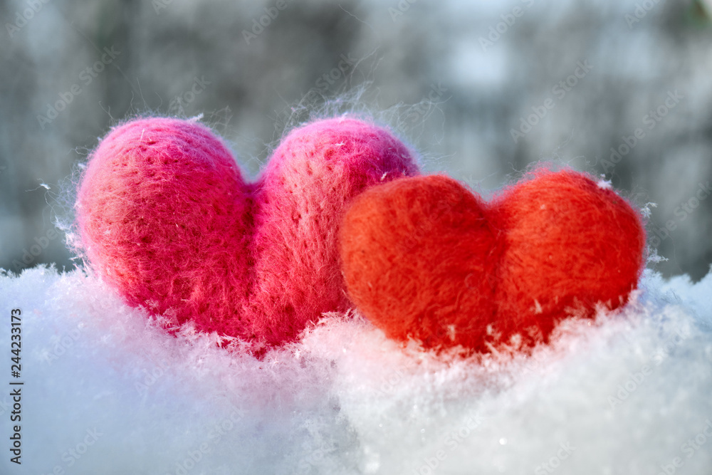 Fototapeta premium Two wool red and pink hearts standing on the white fluffy snow