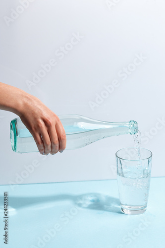 Female hand pours pure mineral water from a bottle into a glass. Minimalist design. The concept of healthy eating.