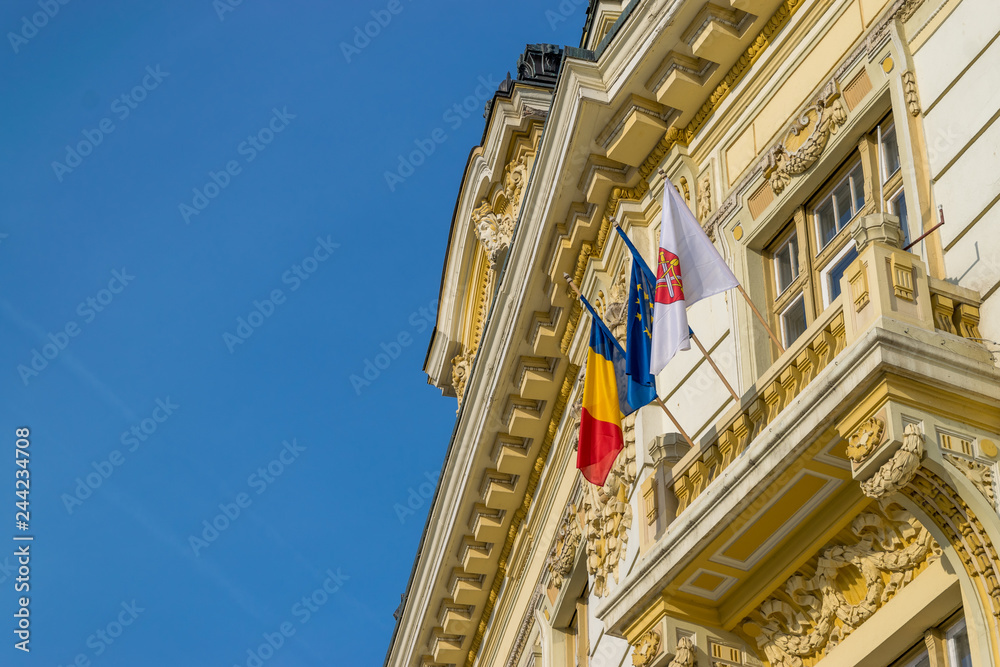 Architectural element and the romanian flag, the EU one,and the flag of the Sibiu municipality