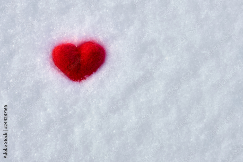 Valentine's day background with a red wool felted heart lying on the white snow