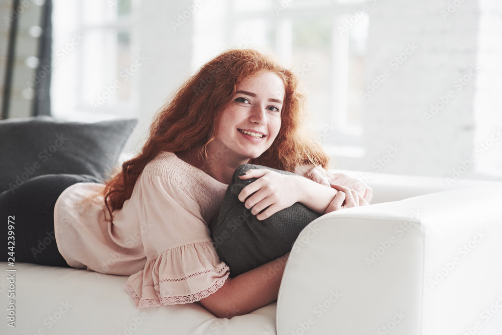 Photo of the young girl laying down on the white sofa and smiling Photo of the young girl laying down on the white sofa and smiling
