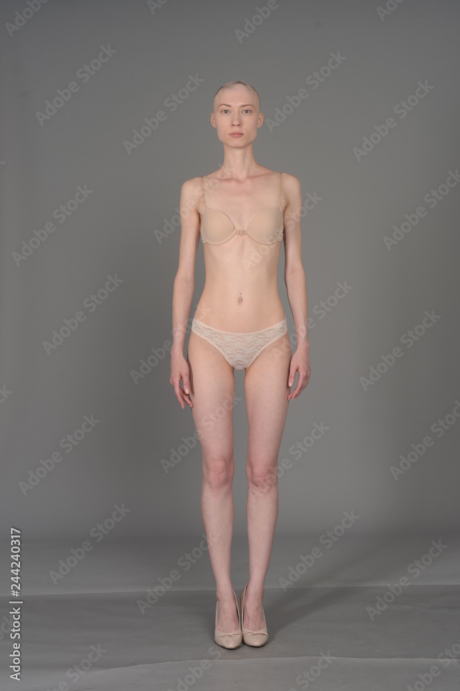 Fototapeta premium bald girl in beige lingerie posing on grey background