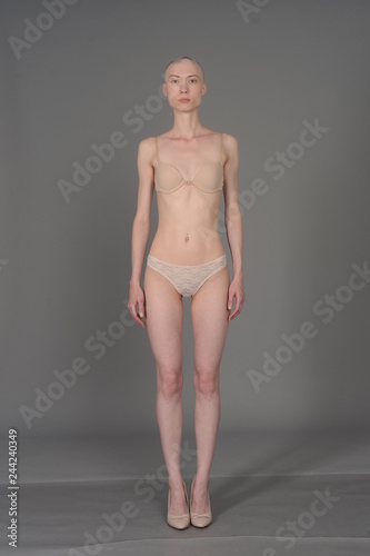 bald girl in beige lingerie posing on grey background
