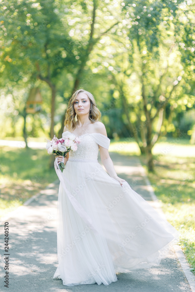 The bride in a white dress in nature in the Park. Photo shoot with a bouquet in the style of fine art.