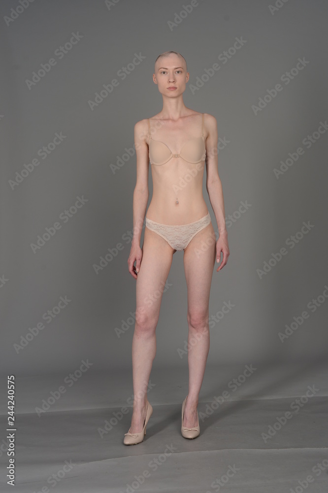 bald girl in beige lingerie posing on grey background bald girl in beige lingerie posing on grey background