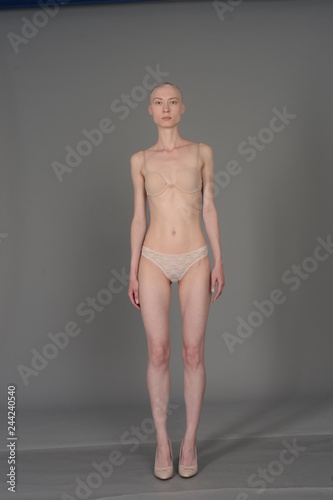 bald girl in beige lingerie posing on grey background